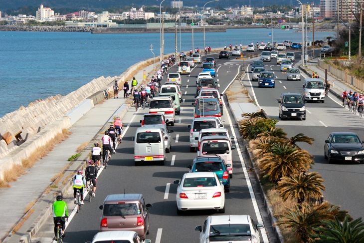 海の向こうに名護市街が見える。道は広いが交通量も多い時間帯だ