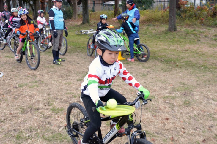 フリスビーのお皿の上のボールを落とさないように自転車に乗る